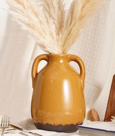 a brown vase with some feathers in it on a table next to silverware and utensils