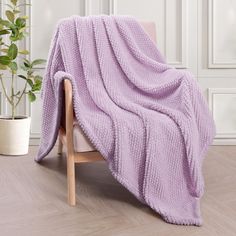 a purple blanket sitting on top of a wooden chair next to a potted plant