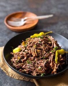 a black bowl filled with shredded meat and green peppers