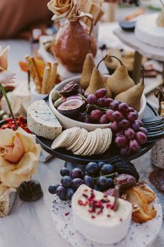 an assortment of cheeses, crackers and grapes on a table with flowers in the background