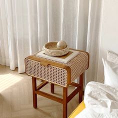 a wicker tray with a hat on it sits next to a white curtained window