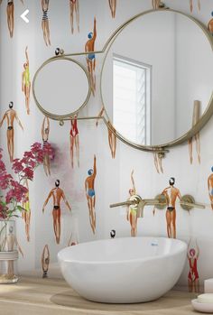 a bathroom sink sitting under a mirror next to a wall paper with people on it