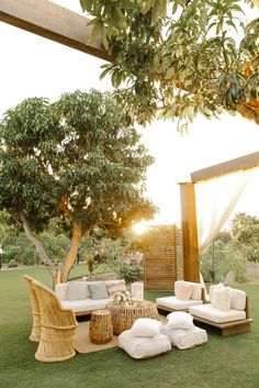 an outdoor seating area with wicker furniture and pillows on the grass under a tree