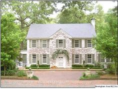 a large white brick house surrounded by trees and bushes with a dog laying in the front yard