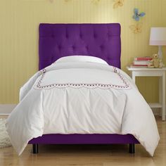 a bed with a purple headboard and white comforter on it's side