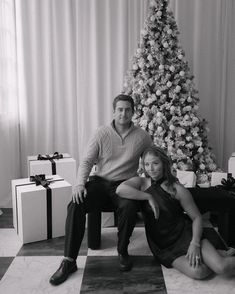 a man and woman sitting in front of a christmas tree