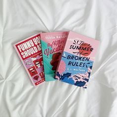 three books are laying on top of a white bed sheet, one is pink and the other is blue