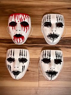 four masks with different designs on them sitting on a wooden surface in front of a wood wall