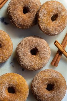 six cinnamon donuts on a plate with cinnamon sticks