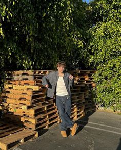 a man standing next to stacks of wooden pallets in front of some green trees