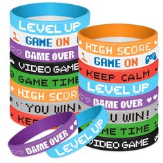 several bracelets with words on them are stacked in different colors and designs, one has a game over wristband