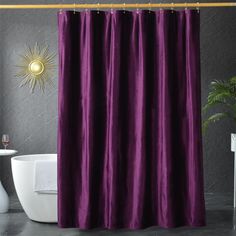 a purple shower curtain in a bathroom next to a white toilet and sink with a gold sunburst on the wall