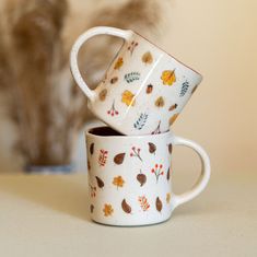 two coffee mugs sitting next to each other on top of a white table with a cat in the background