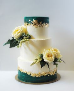 a three tiered white and green wedding cake with flowers on the top, sitting on a table