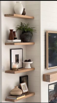 three wooden shelves with pictures and vases on them in the corner of a room