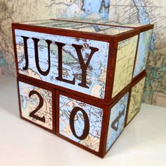 a wooden block with the word july on it and map in the backgroud