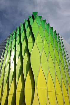 an unusual building with green and yellow designs on it's side against a blue sky