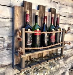 several bottles of wine are sitting on a wooden shelf with rope and glass holders attached to it