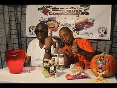 two men sitting at a table with drinks and candy in front of them, posing for the camera