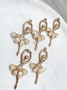 six pairs of gold tone ballet charms on a white plate with crystal accents and pearls