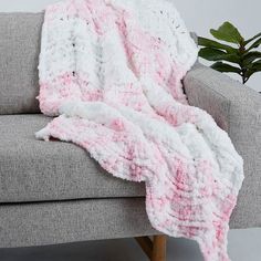 a pink and white crocheted blanket sitting on top of a couch next to a potted plant