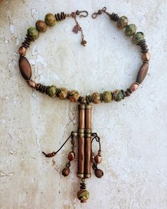 This necklace features an authentic vintage Tibetan Needle Box re-purposed into a piece of unique statement jewelry. I did not envision the piece to be overly colorful so I teamed up the copper patina on the pendant with the green, mustard brown and copper shades of the Kabamba Rhyolite Jasper stone beads. These beads are chunky and heavy - each one being 20mm wide so it gives the necklace a lot of oomph and character. The wood and copper accents add texture to the necklace and the Bronzite stone pebble beads tie the colors and ground the entire piece. I retained the authentic bells that came with the pendant (they hung on very worn out and frayed leather cords on either sides of the needle box) and restrung them in cow-hide leather cords along with copper accents to give the necklace move Rustic One-of-a-kind Festival Necklaces, One Of A Kind Bronze Necklace For Festival, One Of A Kind Vintage Brown Jewelry, Unique Bronze Necklace For Festivals, Vintage Brass Necklaces For Rituals, Artisan Bronze Necklace For Festival, Bronze Hand Wrapped Bohemian Necklace, Rustic Patina Jewelry For Festival, Unique One-of-a-kind Copper Necklace