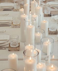 many white candles are lit on a table with place settings and silverware in front of them