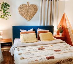 a bed with pillows and blankets on it in front of a wall hanging heart shaped plant