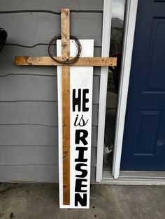 a wooden cross with the words he is risen hanging from it's side in front of a door