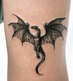 a black dragon tattoo on the side of a woman's thigh, with wings spread out