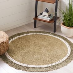 a round rug with fringes on the floor next to a potted plant and bookshelf