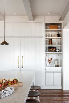 a kitchen with white cabinets and counter tops next to a wood flooring area that has stools on it