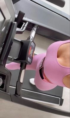 a woman on a treadmill in a pink top and leggings with her cell phone