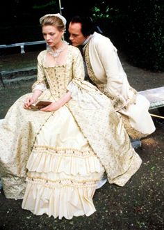 a man and woman sitting on a bench in formal dress, looking at each other