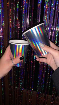 two people holding up holographic cups in front of a window with colorful lights behind them