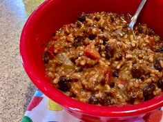 a red bowl filled with chili and beans on top of a table next to a spoon