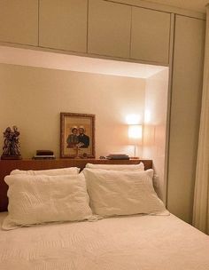 a bed with white sheets and pillows next to a mirror on the wall above it