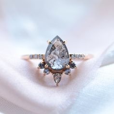 an engagement ring with a large pear shaped diamond surrounded by smaller diamonds on a white cloth