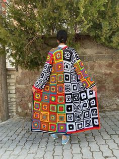 a person standing on a brick walkway wearing a colorful coat with squares in the middle