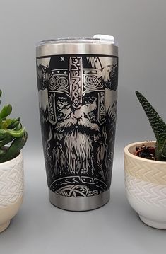 a stainless steel tumbler with an image of a viking warrior on it next to two potted succulents