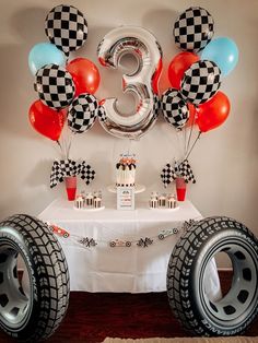 a table topped with balloons and cake next to two large tires on top of a wooden floor