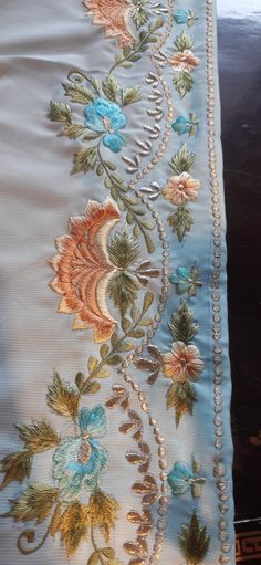 an embroidered fabric with flowers and pearls on the bottom is laying on top of a table