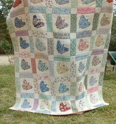 a quilted blanket with butterflies on it sitting in the grass next to a bench