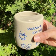 a person holding up a coffee cup in front of some plants and bushes with the words wanna coffee written on it