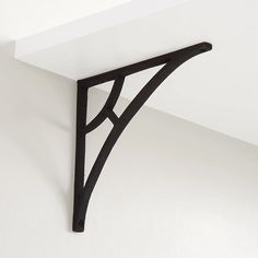 the corner of a shelf with a black bracket on it's side against a white wall