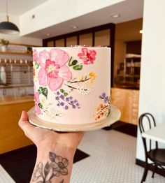 a person holding up a pink cake with flowers on the frosting and icing