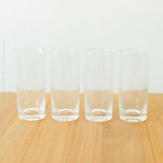 four glasses sitting on top of a wooden table next to each other, with one empty glass in the middle