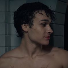 a shirtless young man standing in front of a brick wall with his eyes closed