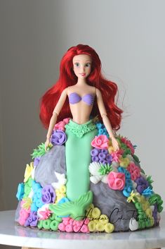 there is a cake made to look like a little mermaid with red hair and flowers on it