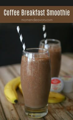 two glasses filled with coffee breakfast smoothie on top of a wooden table next to bananas